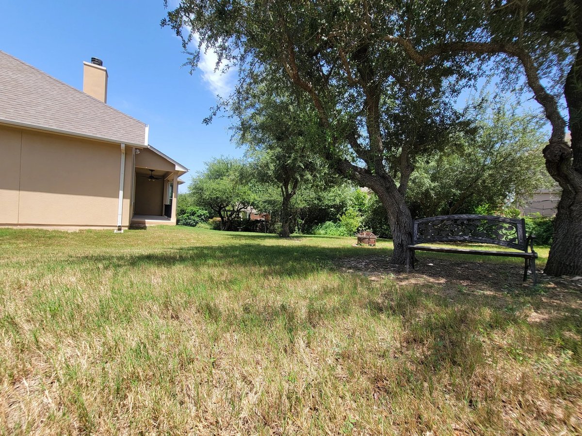Tan residential home with garage on grassy yard under large oak trees on clear sunny day