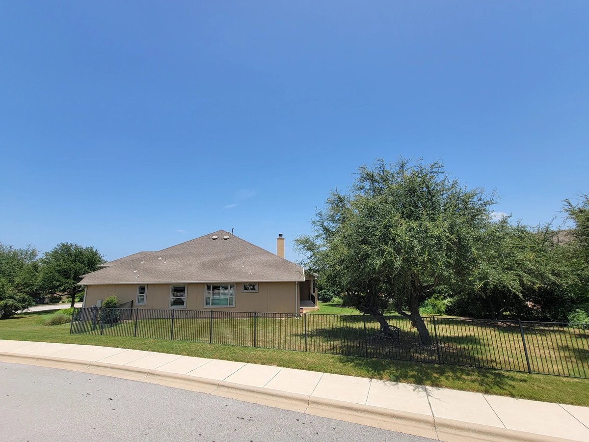 Single-story tan house with black fence in a residential neighborhood under clear blue sky