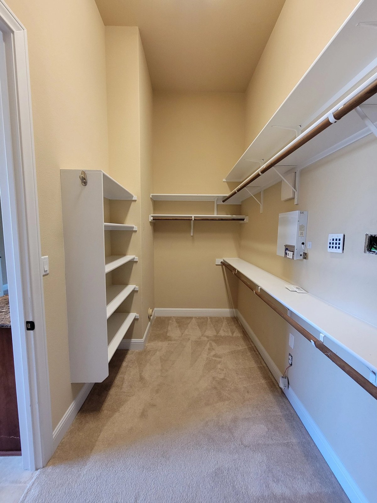 Empty walk-in closet with beige walls, shelving units, hanging rods, and light switches on the right wall
