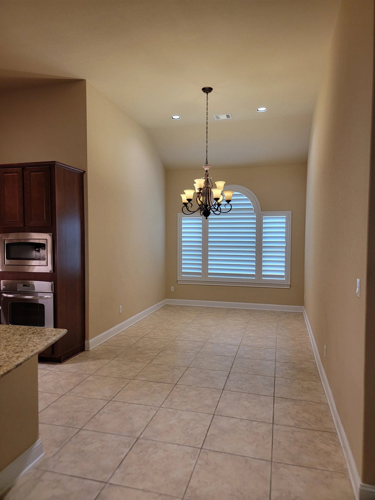 Kitchen and dining area at 16213 Maritime Alps Way — tile flooring, dark wood cabinets, stainless steel appliances, arched window with shutters, pendant lighting in Falconhead West Austin TX 78738. Listed by Gayle Sparkman, Real Estates Of Texas. MLS 8675253