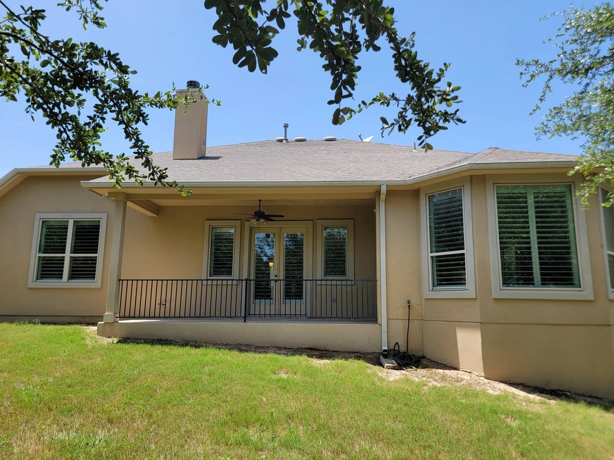Front exterior of beige ranch house with covered porch, multiple windows, and green lawn under clear blue sky