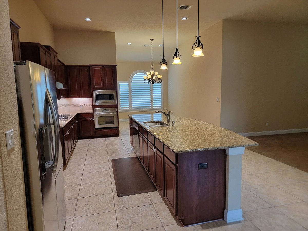Open concept kitchen at 16213 Maritime Alps Way — dark wood cabinetry, granite island countertop, stainless steel appliances, pendant lighting. Falconhead West Austin TX 78738. Real Estates Of Texas listing by Gayle Sparkman. MLS 8675253