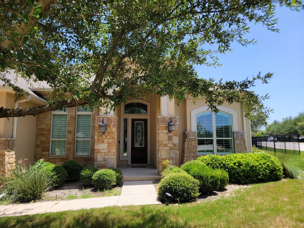 16213 Maritime Alps Way stone and tan brick exterior with mature Live Oak tree canopy overhead, green landscaping, manicured lawn in Falconhead West community, Austin Texas. Real Estates Of Texas — Gayle Sparkman, listing agent. MLS 8675253