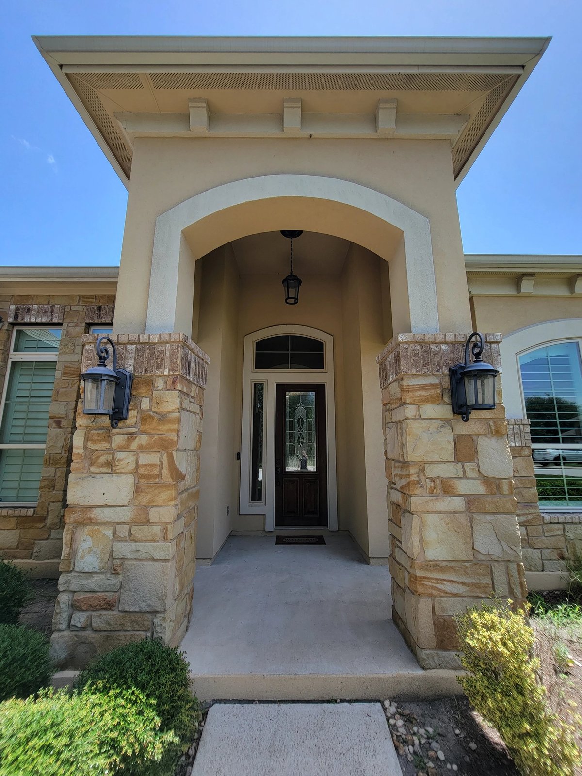Front entrance at 16213 Maritime Alps Way featuring arched doorway with stone columns, black door, lantern sconces — luxury single-story estate in Falconhead West, Austin TX. 4 bedroom 4 bath 2980 sqft corner lot. Real Estates Of Texas, Gayle Sparkman. MLS 8675253