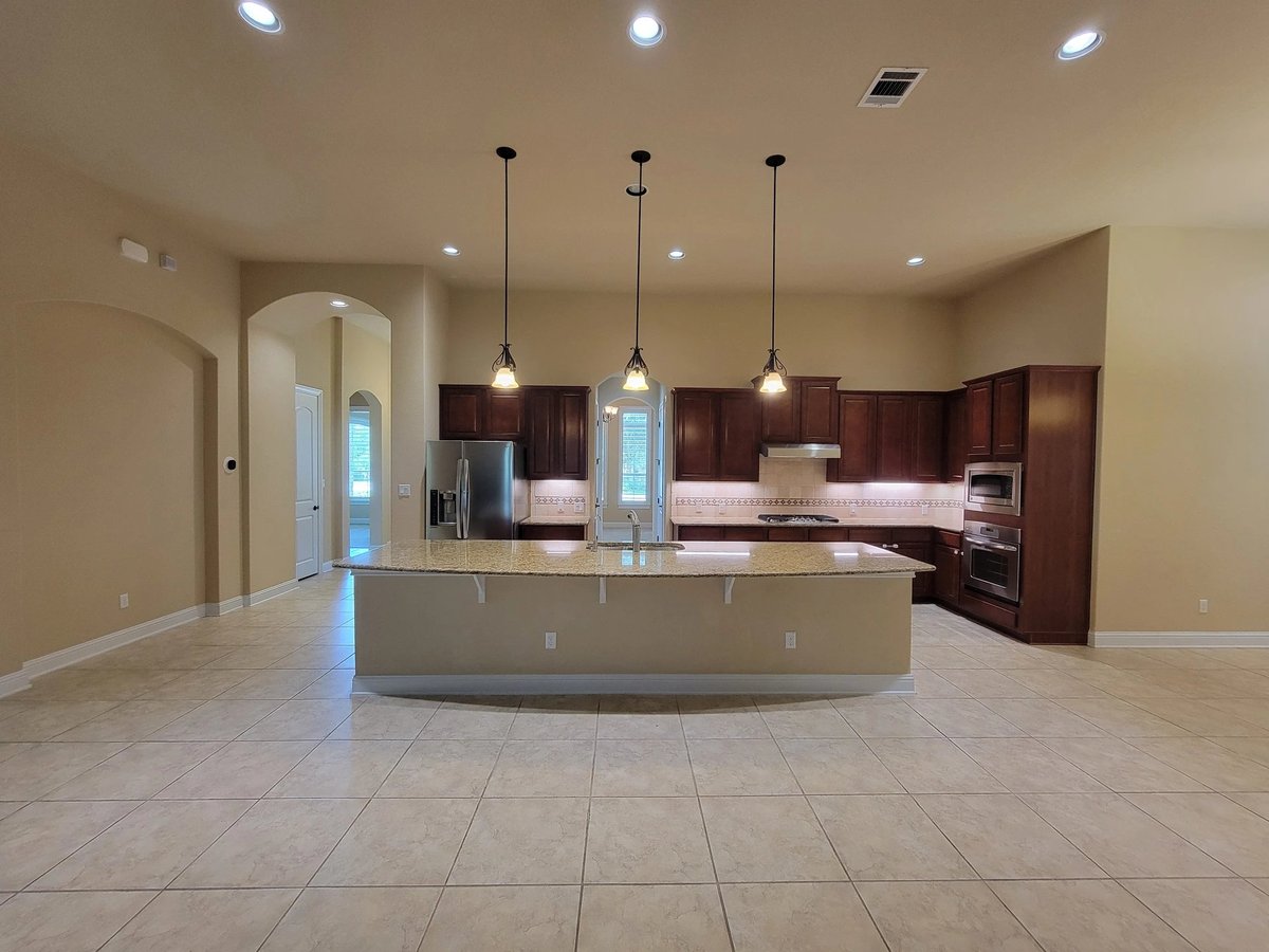 Modern kitchen with large island at 16213 Maritime Alps Way — dark wood cabinets, pendant lighting, tile flooring, open floor plan in Falconhead West Austin TX 78738. Real Estates Of Texas listing by Gayle Sparkman. MLS 8675253