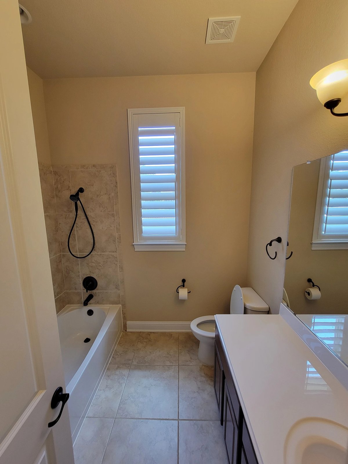 Modern bathroom with dual vanities, shower-tub combo, large mirror, and shuttered windows on pale yellow walls