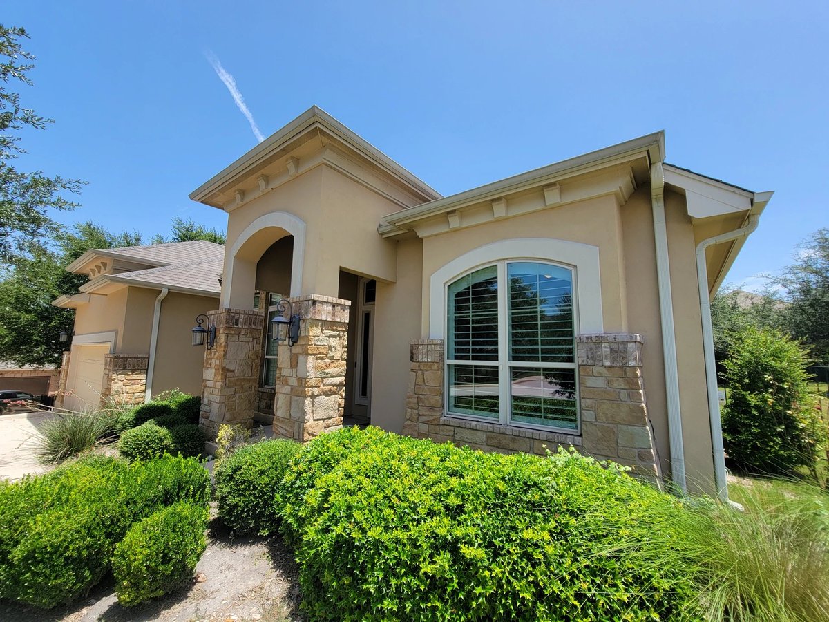 Wide-angle curb appeal of 16213 Maritime Alps Way — modern tan stone home with curved architecture, large windows, landscaped shrubs, Falconhead West largest corner lot in Austin TX. Listed by Gayle Sparkman, Real Estates Of Texas. MLS 8675253 4BR 4BA 2980sqft