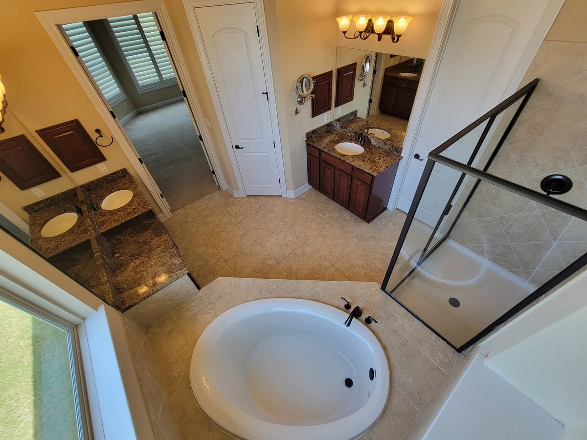 Spacious master bathroom with freestanding white soaking tub, glass shower enclosure, double vanity, and natural lighting from window