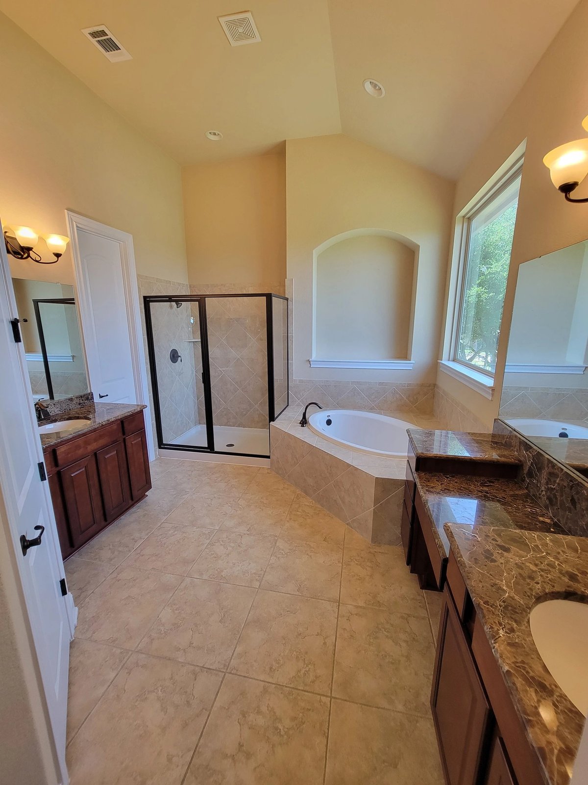 Spacious luxury bathroom with marble countertops, soaking tub, glass shower enclosure, and dual vanities with wood cabinets