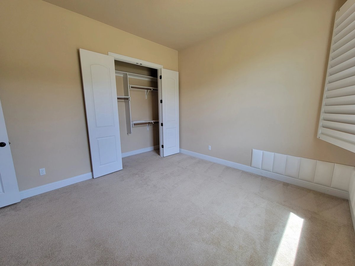 Empty bedroom with beige carpet, white closet doors, window blinds, and light switch on wall