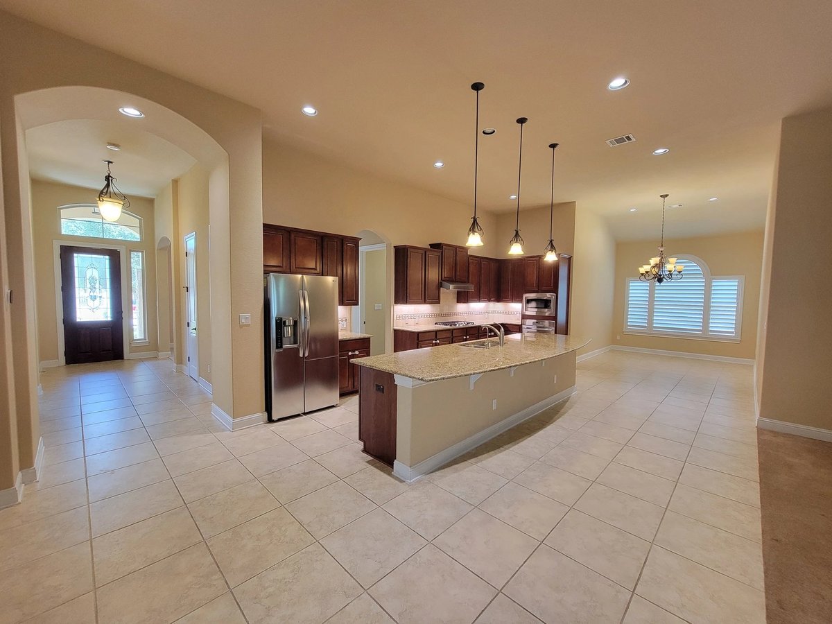 Gourmet kitchen with granite island at 16213 Maritime Alps Way — dark wood cabinetry, stainless steel appliances, pendant lighting, open floor plan with tiled flooring. Falconhead West Austin TX 78738. Real Estates Of Texas, Gayle Sparkman. MLS 8675253